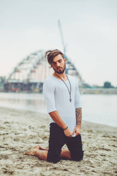 istock Handsome man kneeling on the sand by the river 909291400