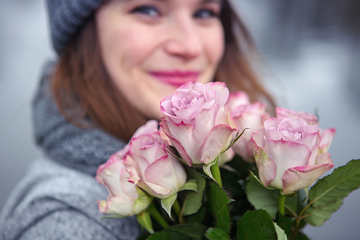 portrait of beautiful young woman outdoors with bouquet of pink roses