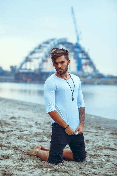 istock Handsome man kneeling on the sand by the river 909291952