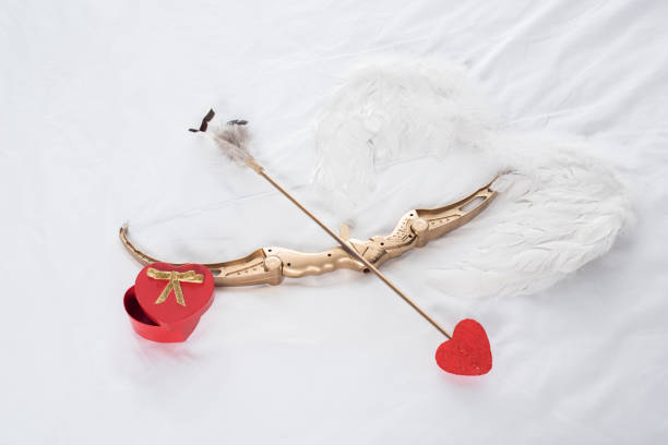 top view of gift box, wings, bow and arrow on white bed