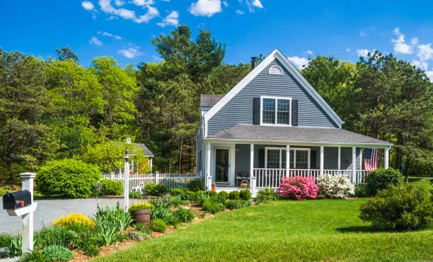 An American flag flies from the open porch and gardens surround a small  single family home on a Spring afternoon on Cape Cod on the Massachusetts coast.