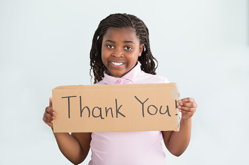 Close-up Of A Smiling African Girl Holding Thank You Sign Against White Background