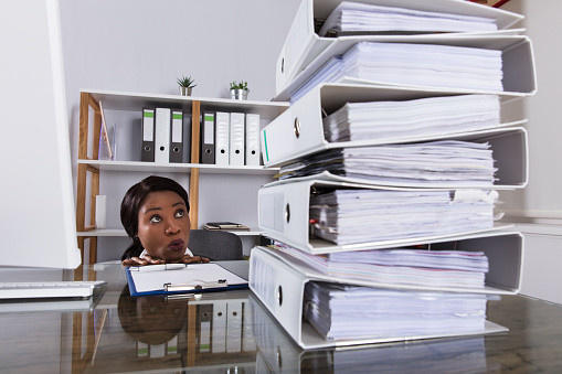 Young African Woman Looking At Stack Of Folders On Desk In Office
