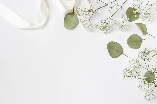 Styled stock photo. Feminine wedding desktop mockup with baby's breath Gypsophila flowers, dry green eucalyptus leaves, satin ribbon and white background. Empty space. Top view. Picture for blog