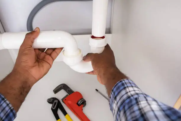 Photo of Plumber Fitting Sink Pipe In Kitchen