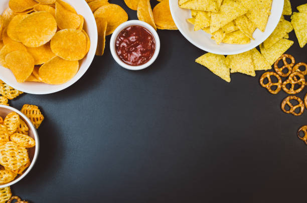 istock Potato chips and snacks on black slate table, top view 909323932