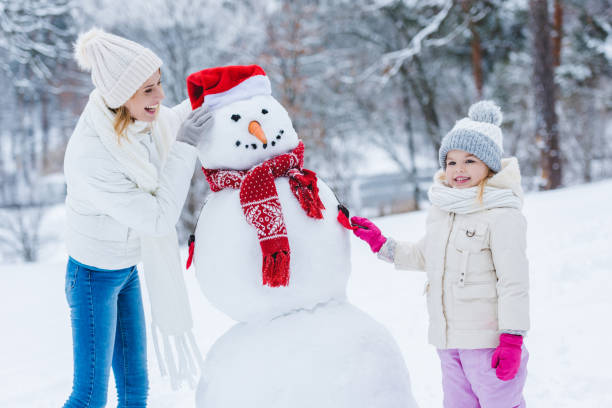 istock mother and daughter making snowman together in winter forest 909329892