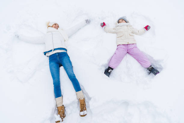 istock mother and daughter making snow angels and smiling 909339966