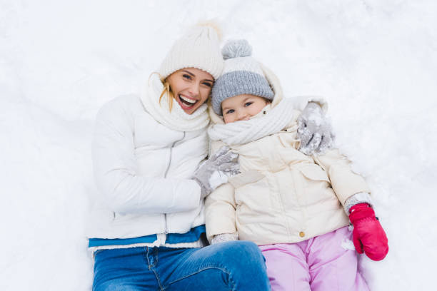 istock mother and daughter smiling at camera while lying together in snow 909343054