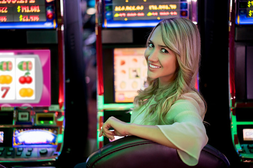Happy woman playing at the casino on the slot machines and looking at the camera smiling - lifestyle concepts