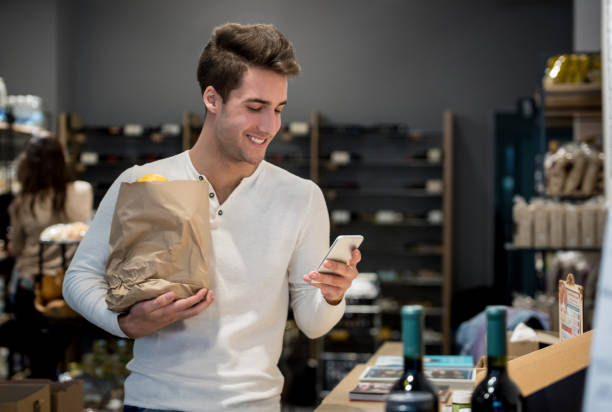 istock Happy customer at a gourmet store looking at his smartphone smiling 909349614