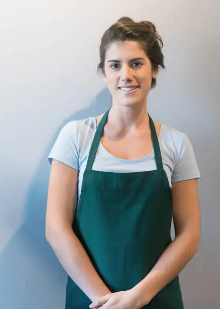 Portrait of female waitress looking at camera smiling wearing a green apron