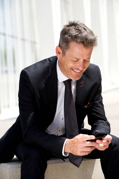 istock Businessman sitting and smiling holding mobile phone 909350192