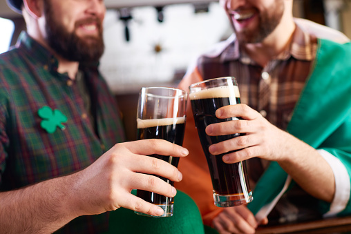 Close-up of cheerful men in costume clinking beer glasses while celebrating St Patrick day