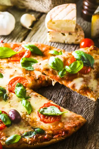 Pizza on wood with ingredients. Pizza slice with cheese, tomatoes and basil. Rustic italian pizza