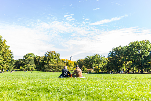 New York City: Manhattan NYC Central park with couple people sitting having picnic in front of buildings skyscrapers view on great lawn grass meadow in autumn fall season