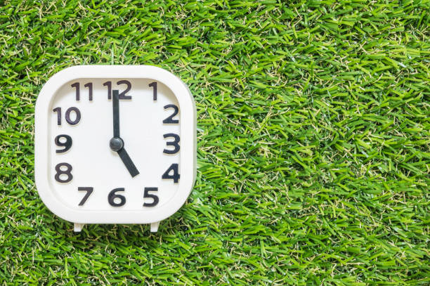 istock Closeup white clock for decorate in 5 o'clock on green artificial grass floor textured background with copy space 909373572