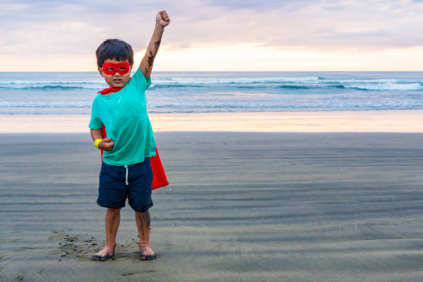 młody chłopak przebrany za superbohatera pokazujący, jak silny jest - murawai beach zdjęcia i obrazy z banku zdjęć