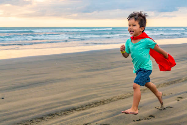 młody chłopak przebrany za super bohatera biegającego po plaży - murawai beach zdjęcia i obrazy z banku zdjęć