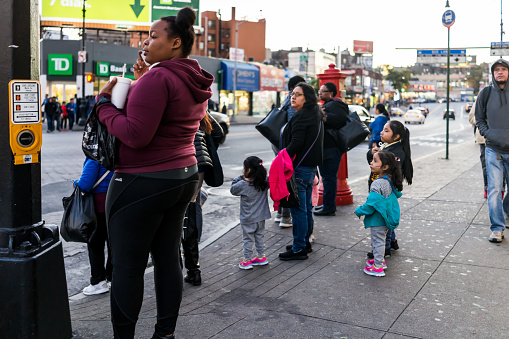 Bronx: People family waiting to cross street in Fordham Heights center, New York City, NYC in evening