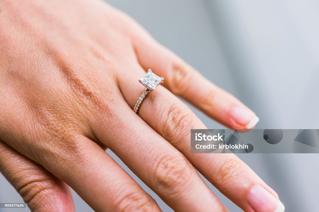 Macro closeup of princess cut diamond engagement ring on woman's female hand showing detail and texture Engagement Ring Stock Photo