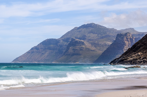Beautiful view of mountains near Hout Bay, Cape Town, South Africa, seen from Noordhoek Long Beach. White sand beach and waves with spray. Noordhoek Beach is a popular tourist destination.