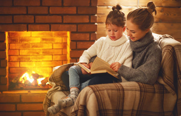 fille famille heureuse pour la mère et l’enfant lire un livre le soir d’hiver près de cheminée - 7652 photos et images de collection