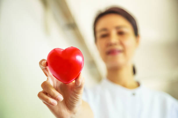 istock Red heart held by smiling female nurse's hand, representing giving effort high quality service mind to patient. Professional, Specialist in white uniform concept 909395924