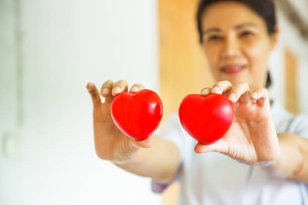 istock Two Red Hearts held by smiling female nurse's hands, representing giving effort high quality service mind to patient. Professional, Specialist in white uniform concept 909395960