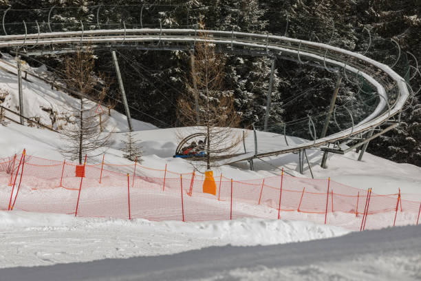 istock Winter bobsled track in the forest in Dolomites. Two Boys ridings a bobsleigh sitting on a blue truck 909399306