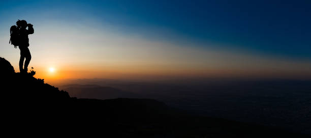 istock Silhouette of a standing man with binocular on the mountain peak 909407030