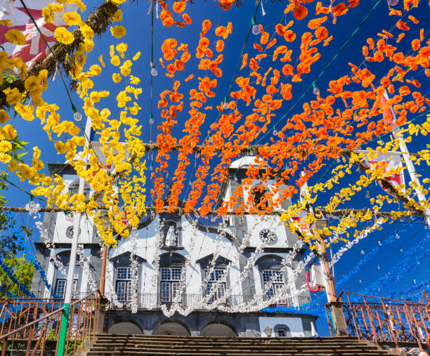 Brilliant blue sky above the Church of our Lady of Monte Decorate yellow, orange, blue and white flowers strung up leading to the Church of our Lady of Monte in Funchal, Portugal. funchal stock pictures, royalty-free photos & images