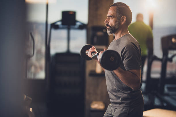 aktiven senior mann stärke mit langhantel in einem fitnessstudio zu trainieren. - bizeps fotos stock-fotos und bilder
