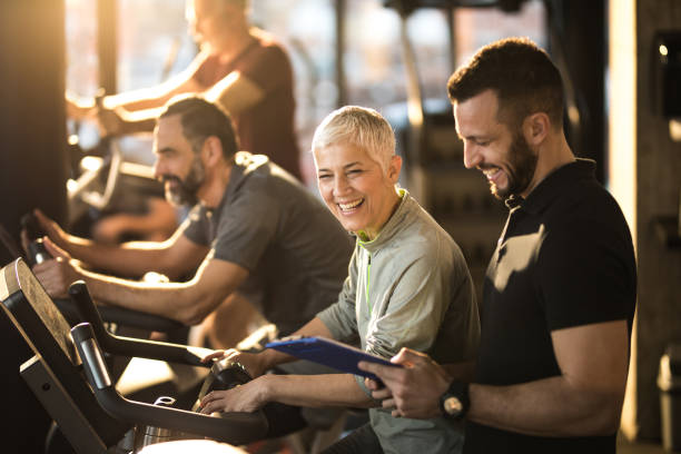 Happy senior woman having fun with her coach on exercising class in a gym. Group of athletic seniors having a exercising class in a health club. Focus is on senior woman having fun with her fitness instructor. fitness instructor stock pictures, royalty-free photos & images