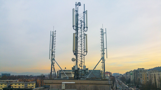 Cellular network antenna radiating and broadcasting strong power signal waves over the city on a building roof with telecommunication mast