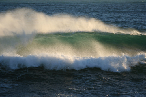 Powerful storm generated ocean swell exploding dangerously on the shoreline with soft golden sky