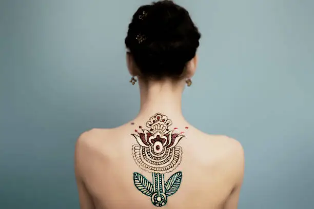 Hennaed beautiful female back, mandala flower image, traditional Indian, Pakistani, African, Oriental motivs, cultural traditions, customs. Mehendi made of brown, red, green henna paste. Professional