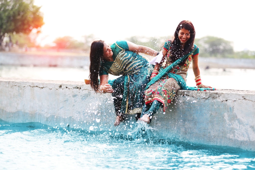 Two young woman doing fun in lake water and also sitting on a wall of lake.