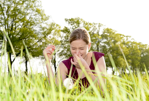 Beautiful young woman with dandelion lying on grass