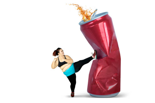Diet concept. Overweight woman kicking a can of soft drink. Isolated on white background