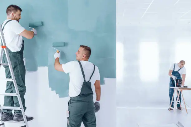 Photo of Men painting empty home interior