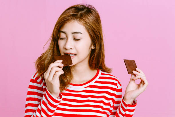 Beautiful woman eating dark chocolate on pink background stock photo