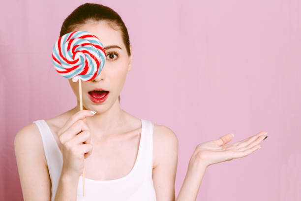 istock Woman holding a lollipop on pink background 909475122