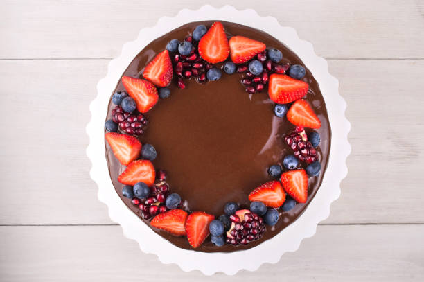 gâteau d’anniversaire au chocolat avec des fraises, bleuets et grenat sur une table en bois blanc. - gâteau danniversaire photos et images de collection