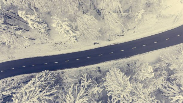 Aerial view of road through a winter forest. Snow covered landscape.