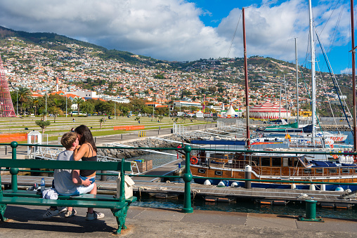 Funchal Madeira, Portugal - December 18, 2017: sailing ships in the harbor of Funchal, Madeira. View to the city and hills. in the foregrond a loving young couple, enjoying the warm december sun
