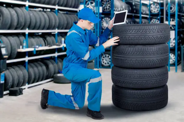 Male mechanic holding a digital tablet and checking a pile of tyre in the workshop