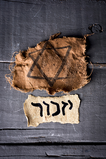 high angle view of a ragged jewish badge and a yellowish piece of paper with the word yizkor, remember in hebrew and the name of a prayer in memory of deceased beloveds, on a rustic wooden surface