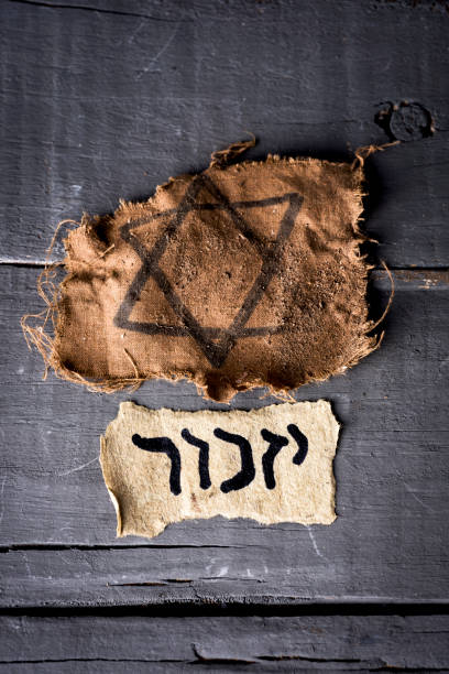 jewish badge and hebrew word yizkor, for remember high angle view of a ragged jewish badge and a yellowish piece of paper with the word yizkor, remember in hebrew and the name of a prayer in memory of deceased beloveds, on a rustic wooden surface nazism photos stock pictures, royalty-free photos & images