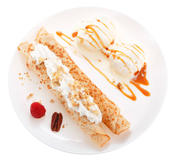 istock Serving pancakes with ice cream, nuts, raspberry and whipped cream on the plate. Decorated with caramel syrup. Isolated on white background. Top view. 909486562